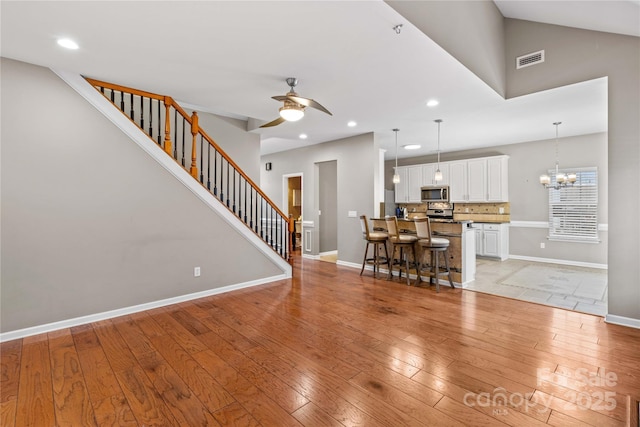 unfurnished living room featuring vaulted ceiling, ceiling fan with notable chandelier, and light hardwood / wood-style floors