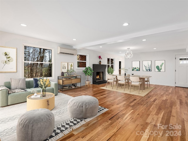 living room with a fireplace, a wall unit AC, wood-type flooring, beamed ceiling, and a chandelier