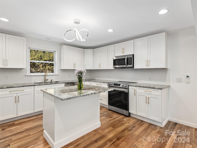 kitchen with light stone countertops, white cabinets, stainless steel appliances, light hardwood / wood-style floors, and sink