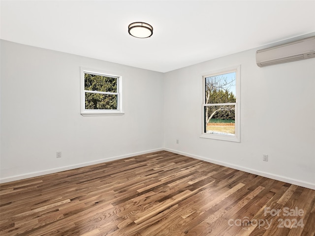 unfurnished room with a wall mounted AC, a healthy amount of sunlight, and hardwood / wood-style floors