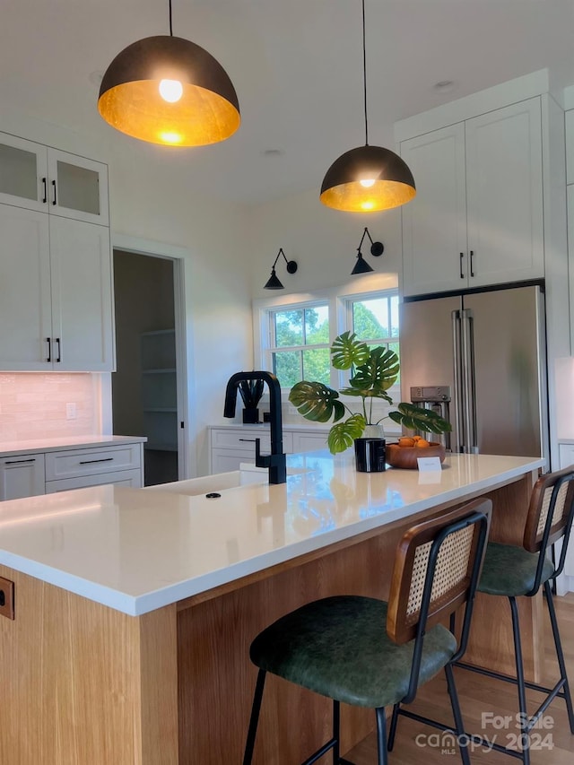 kitchen with hanging light fixtures, high end fridge, hardwood / wood-style floors, a breakfast bar, and white cabinetry