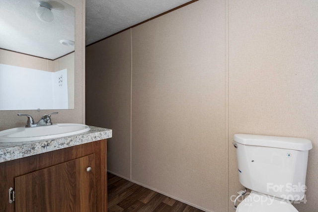 bathroom with toilet, vanity with extensive cabinet space, a textured ceiling, and wood-type flooring