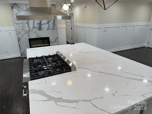 kitchen with ornamental molding, light stone counters, wall chimney exhaust hood, and dark hardwood / wood-style flooring