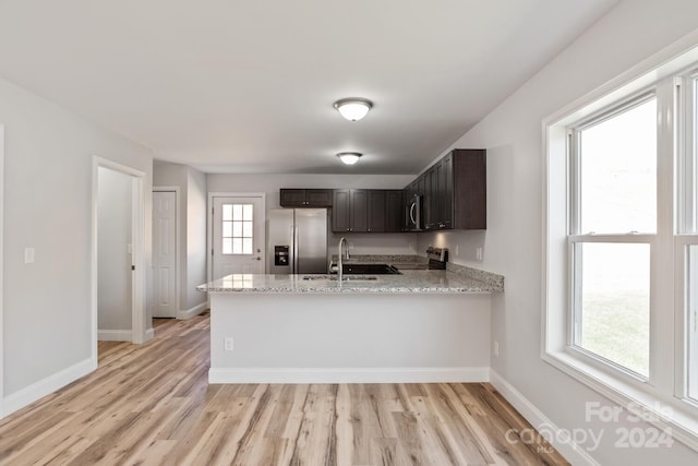 kitchen with dark brown cabinetry, sink, light stone counters, kitchen peninsula, and stainless steel appliances