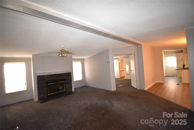 unfurnished living room with ceiling fan, a tiled fireplace, dark carpet, and a textured ceiling