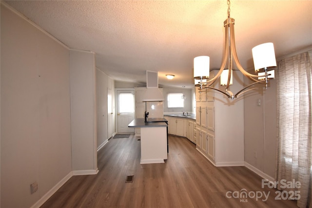 kitchen with decorative light fixtures, dark wood-type flooring, white cabinetry, sink, and range hood