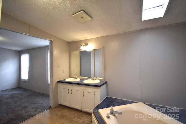 bathroom featuring a tub to relax in, vanity, a skylight, and a textured ceiling