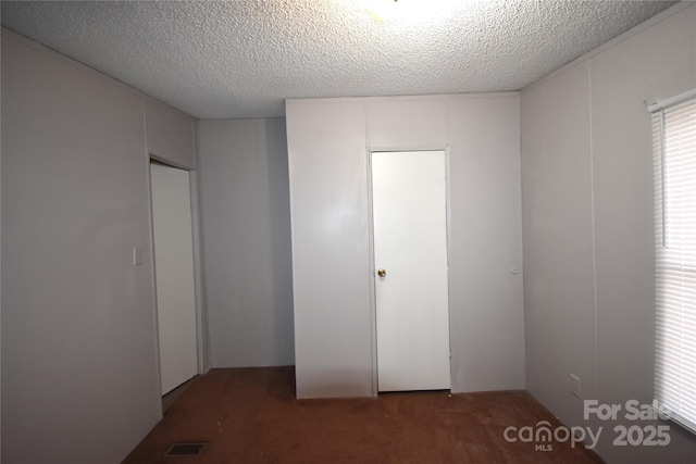 unfurnished bedroom featuring dark carpet, a textured ceiling, and a closet