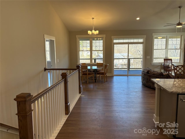 interior space featuring vaulted ceiling, ceiling fan with notable chandelier, light stone countertops, pendant lighting, and dark wood-type flooring