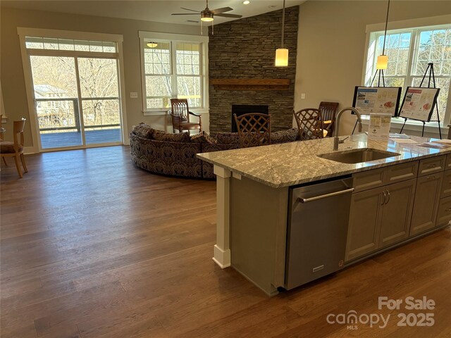 kitchen with sink, a fireplace, dishwasher, hanging light fixtures, and light stone countertops