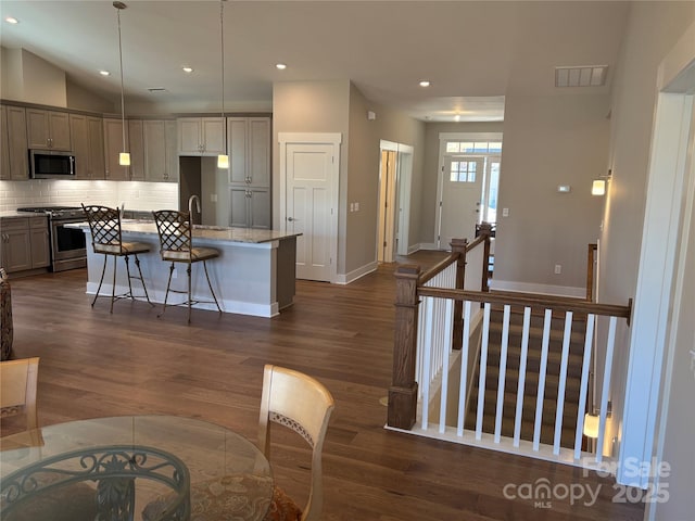 kitchen featuring light stone countertops, stainless steel appliances, an island with sink, backsplash, and sink