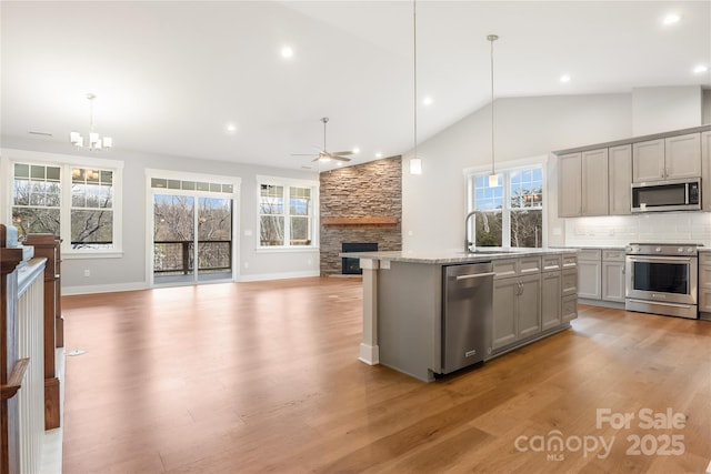 kitchen with open floor plan, a stone fireplace, appliances with stainless steel finishes, a healthy amount of sunlight, and gray cabinetry