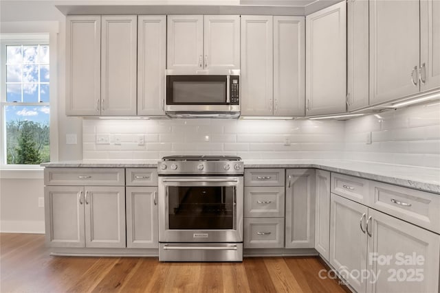 kitchen featuring decorative backsplash, light stone counters, light wood-style floors, and stainless steel appliances