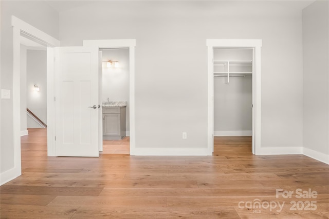 unfurnished bedroom featuring a walk in closet, light wood-style floors, a closet, and baseboards