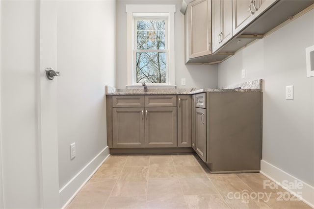 laundry room with baseboards, a sink, and cabinet space