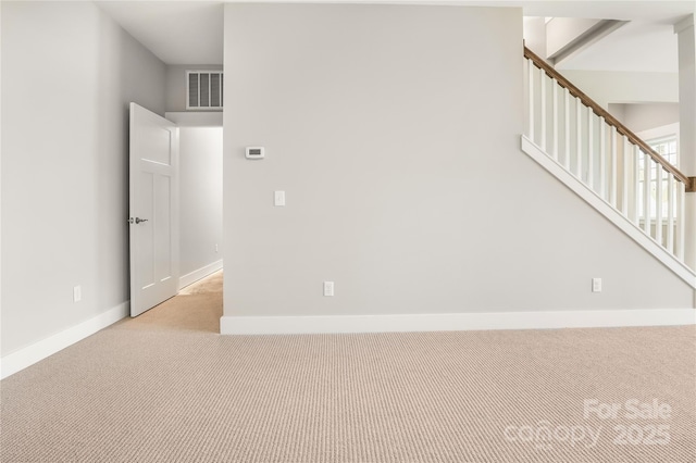 empty room featuring light colored carpet, baseboards, visible vents, and stairway
