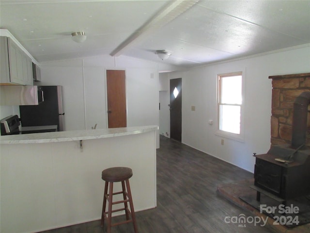 kitchen with stainless steel appliances, vaulted ceiling with beams, a wood stove, a kitchen breakfast bar, and kitchen peninsula