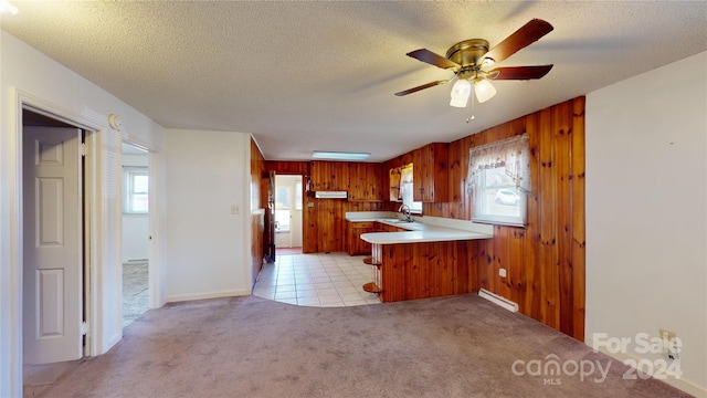 kitchen featuring wood walls, ceiling fan, kitchen peninsula, light carpet, and sink