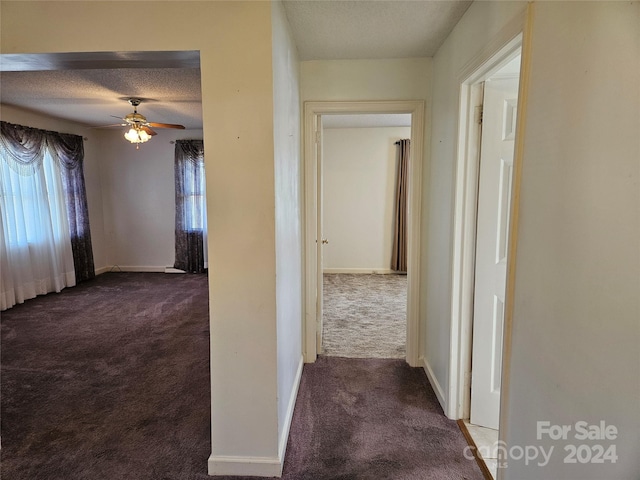 hallway with dark colored carpet and a textured ceiling