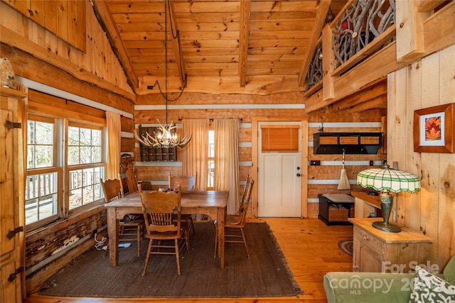 dining space with wooden walls, high vaulted ceiling, a notable chandelier, and light wood-type flooring