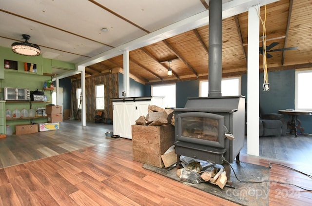 living room with lofted ceiling with beams, dark wood-type flooring, a wood stove, and a wealth of natural light