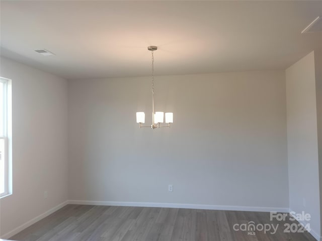 empty room with hardwood / wood-style flooring and an inviting chandelier