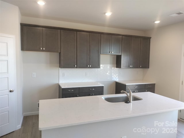 kitchen with hardwood / wood-style floors, backsplash, a center island with sink, and sink