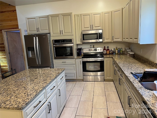 kitchen featuring stainless steel appliances, light tile floors, sink, and light stone counters