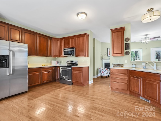 kitchen with appliances with stainless steel finishes, sink, light wood-type flooring, kitchen peninsula, and ceiling fan