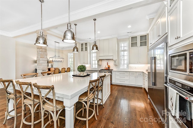 kitchen with a breakfast bar, decorative light fixtures, dark hardwood / wood-style floors, and built in appliances