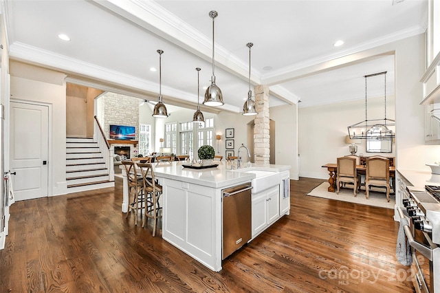 kitchen featuring dark wood-type flooring, appliances with stainless steel finishes, white cabinets, an island with sink, and hanging light fixtures