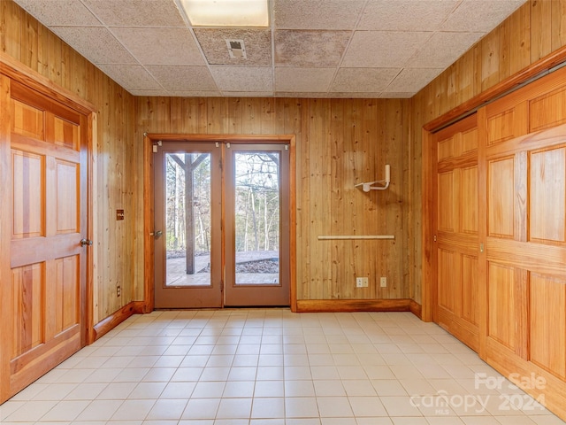 entryway featuring french doors, a drop ceiling, wooden walls, and light tile patterned flooring