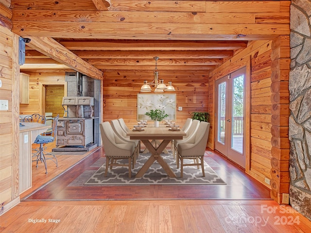 unfurnished dining area featuring a wood stove, french doors, beamed ceiling, wood walls, and hardwood / wood-style floors