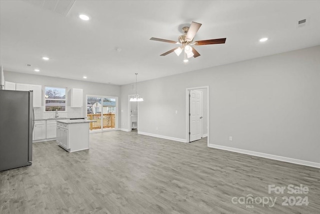 kitchen with backsplash, ceiling fan with notable chandelier, light wood-type flooring, a center island, and stainless steel refrigerator