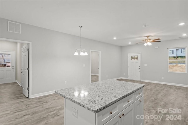 kitchen featuring white cabinets, light hardwood / wood-style floors, decorative light fixtures, ceiling fan with notable chandelier, and a center island