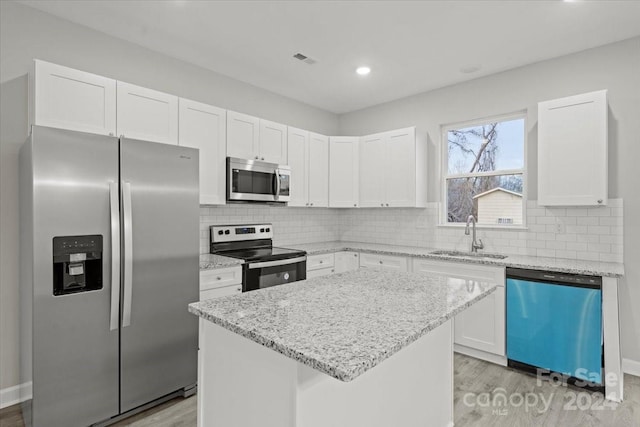 kitchen featuring light wood-type flooring, stainless steel appliances, a kitchen island, and white cabinetry