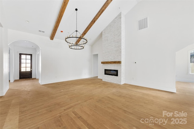 unfurnished living room featuring an inviting chandelier, high vaulted ceiling, light wood-type flooring, a large fireplace, and beam ceiling