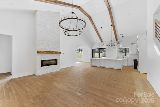 unfurnished living room featuring a stone fireplace, high vaulted ceiling, light hardwood / wood-style floors, and a chandelier