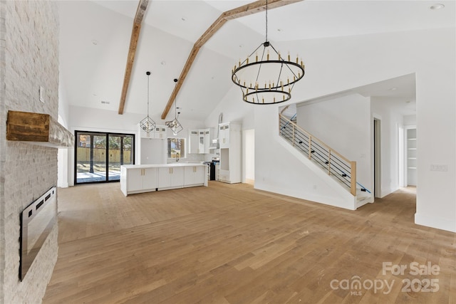 unfurnished living room featuring a fireplace, high vaulted ceiling, a chandelier, beam ceiling, and light hardwood / wood-style flooring