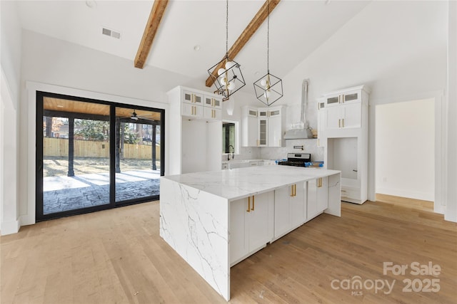 kitchen featuring wall chimney exhaust hood, light stone counters, decorative light fixtures, a center island, and white cabinets