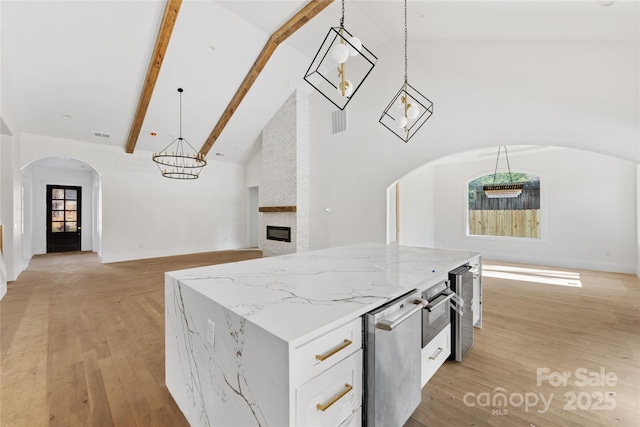 kitchen with white cabinetry, hanging light fixtures, light stone counters, light hardwood / wood-style floors, and a kitchen island