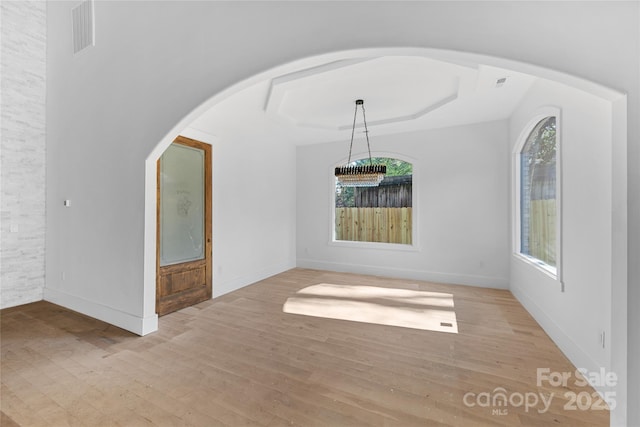 unfurnished dining area featuring a tray ceiling and light hardwood / wood-style flooring