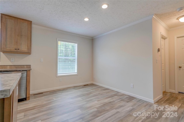 unfurnished dining area with a textured ceiling, crown molding, and light hardwood / wood-style floors