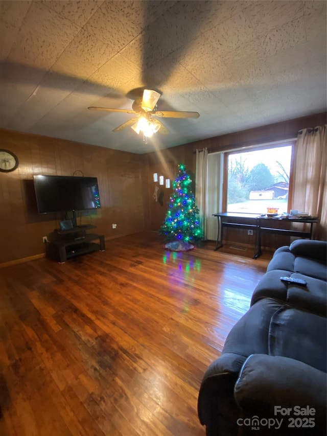 living room featuring hardwood / wood-style flooring, ceiling fan, and wood walls