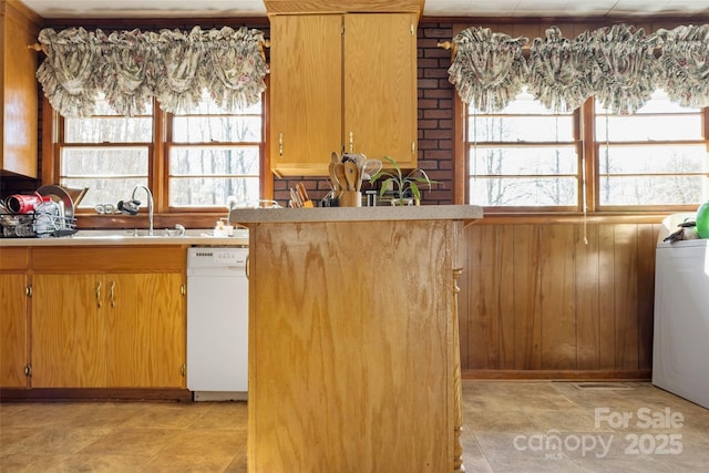 kitchen with wooden walls, white dishwasher, washer / clothes dryer, and sink