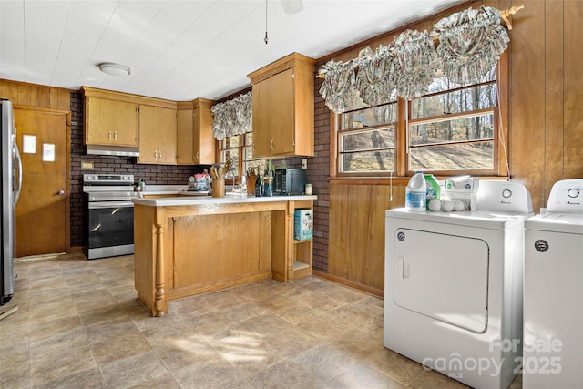 kitchen featuring stainless steel appliances, washing machine and clothes dryer, wooden walls, and kitchen peninsula