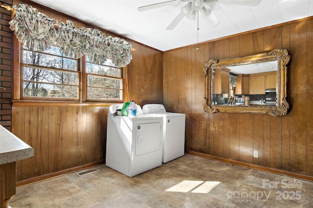 clothes washing area featuring ceiling fan, washing machine and dryer, and wood walls