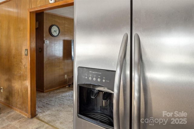 kitchen with light carpet, stainless steel fridge, and wood walls