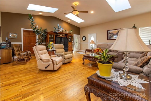 living room featuring light hardwood / wood-style floors, vaulted ceiling with skylight, and ceiling fan