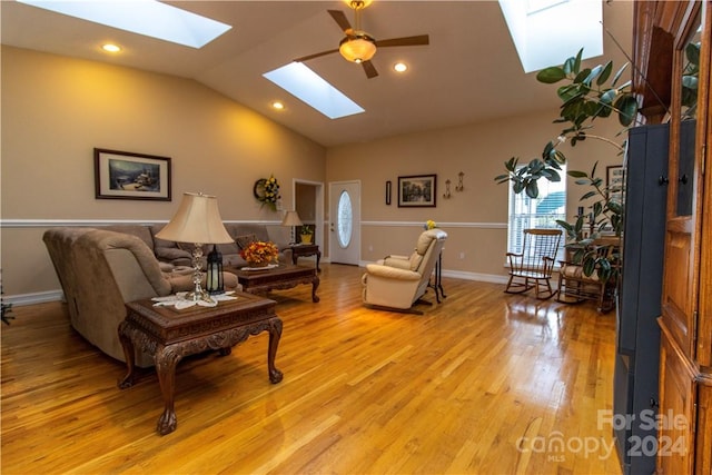 living room featuring vaulted ceiling with skylight, ceiling fan, and light wood-type flooring